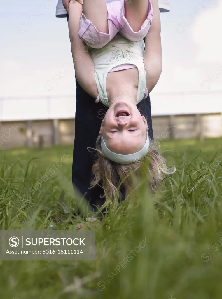 Young girl hanging upside down and mother holding her