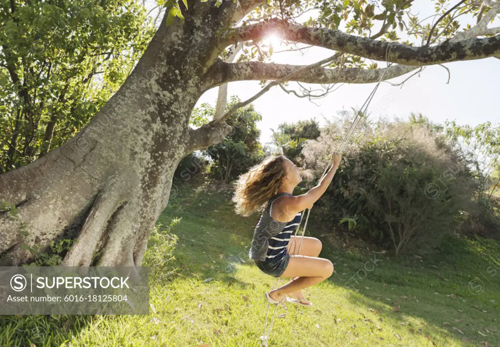 Teenage girl swinging on rope swing tied to big old tree
