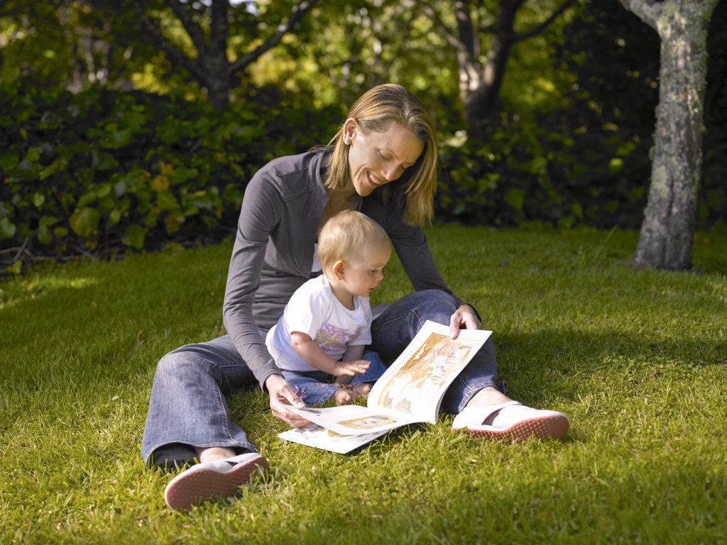 Mother sitting on the grass with little child reading a book to her
