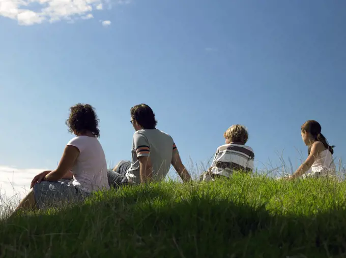 Back view of a group of young people sitting on top of a hill against blue sky