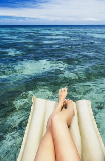 A close up view of legs and feet of a woman lying on lilo floating in tropical water