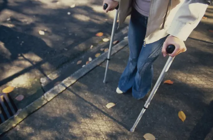 Waist down of disabled woman on crutches walking on the sidewalk