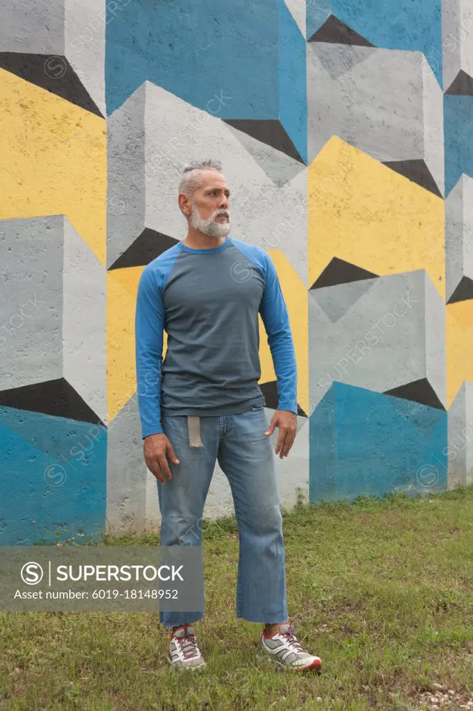 Relaxed stylish gray-haired man in jean and long sleeve flannel with colorful background