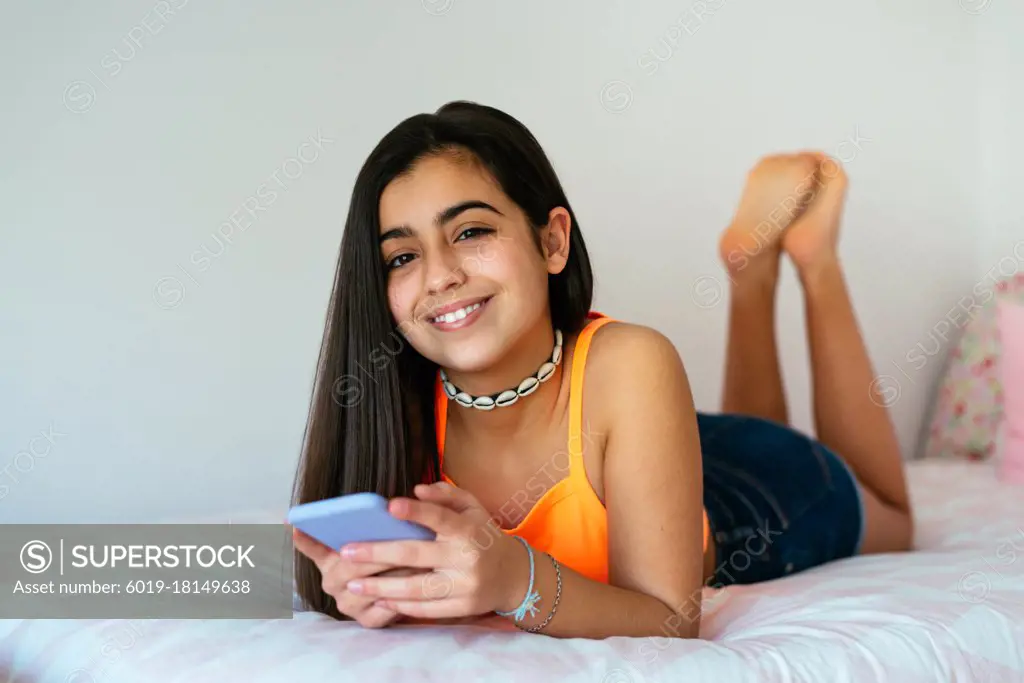 Portrait cheerful teen girl lying in bed and using her smartphone