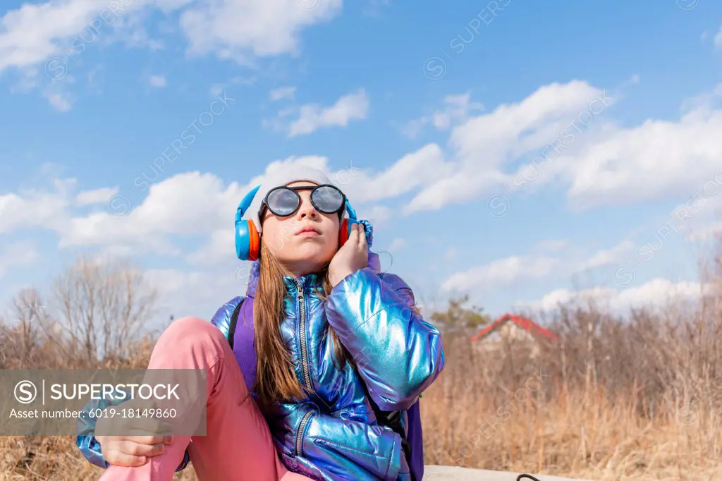 Teenage girl in mirrored sunglasses looks into the sky. Wellness concept. Child listens to music and sings