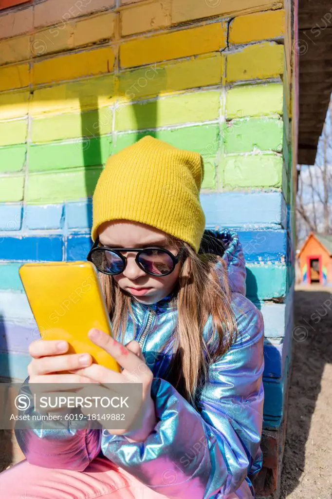 Teenage girl sits outdoors and looks into her smartphone. Concept wellness and technology use child