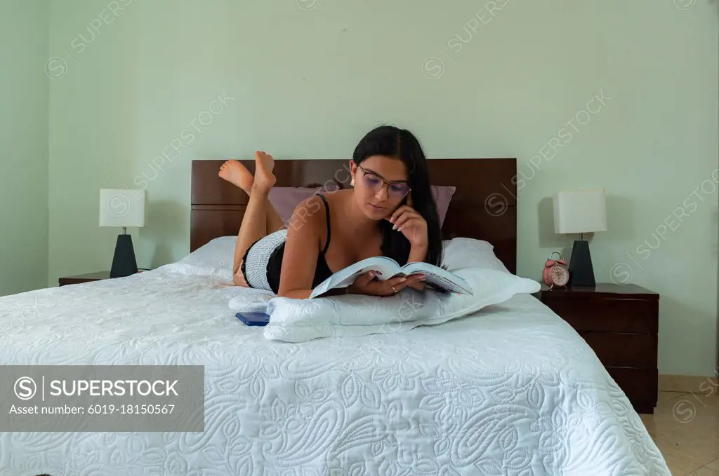 young woman lying in bed reading a book