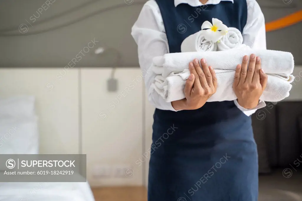 Chambermaid holding stack of fresh towels after cleaning hotel