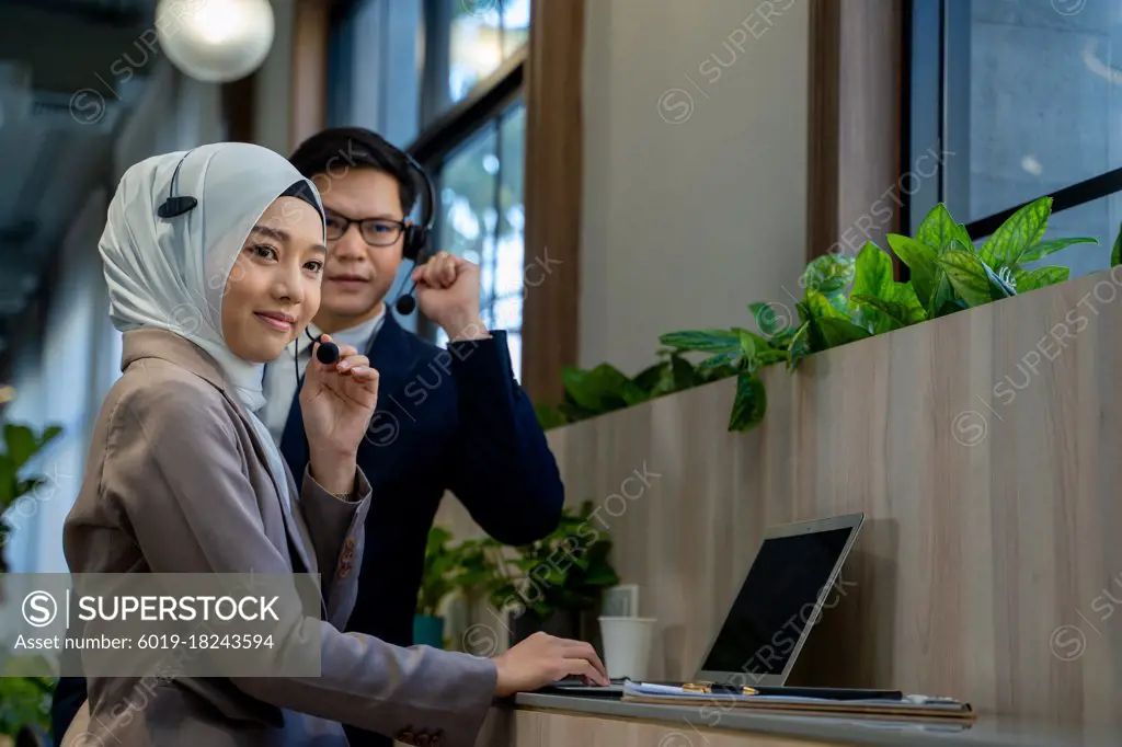 Businessman and Muslim lady employee with headset use laptop
