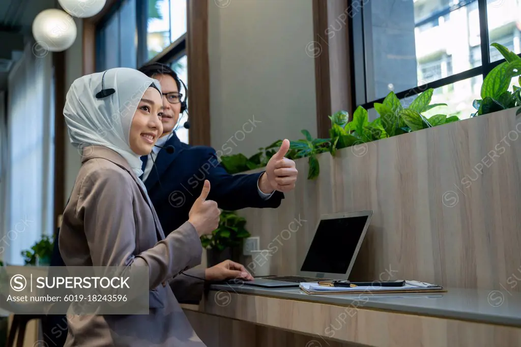 Businessman and Muslim lady employee with headset use laptop