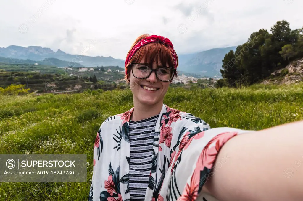 Woman doing a selfie in a meadow looking happy wearing a flowers shirt