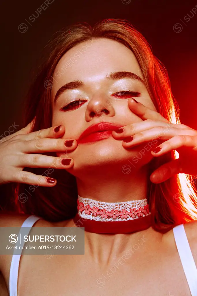 Close-up portrait of beautiful red-haired green-eyed girl with dark trendy makeup: red lips and red eyeshadows, with choker at her neck. Gloomy and sad portrait