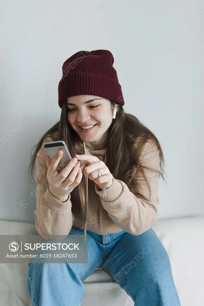 Stylish young woman smiling, using phone, listening to music.