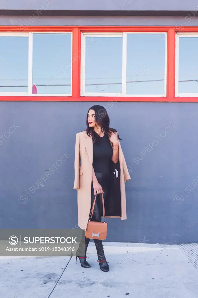 Friendly business woman standing in front of gray wall, orange windows
