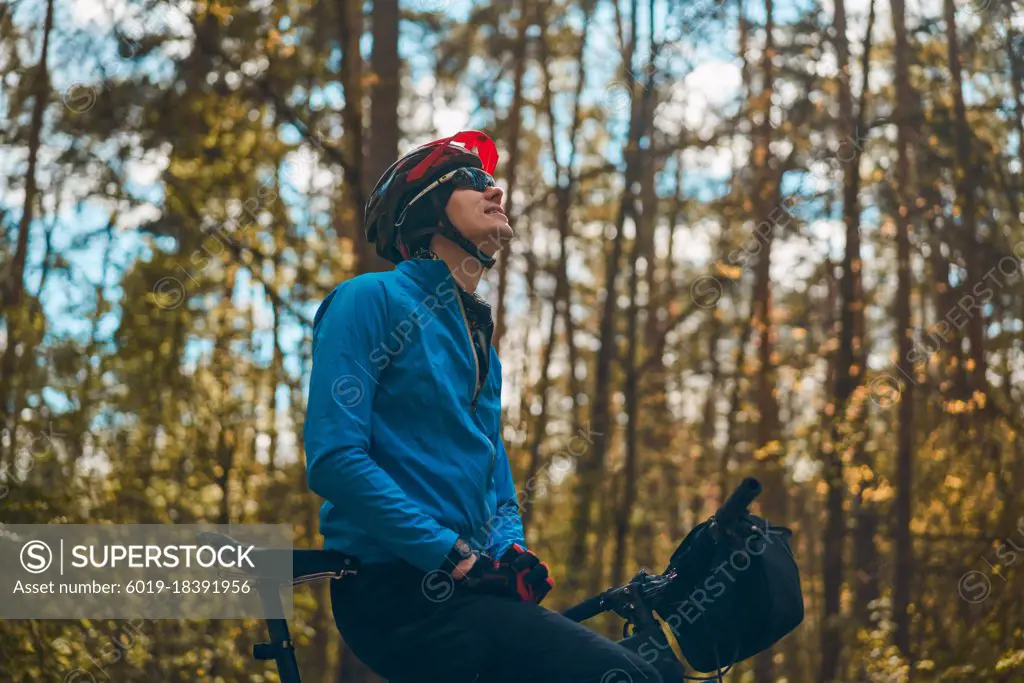 Man wearing bicycle helmet standing in forest, spending free vacation time on a bicycle trip in a forest.