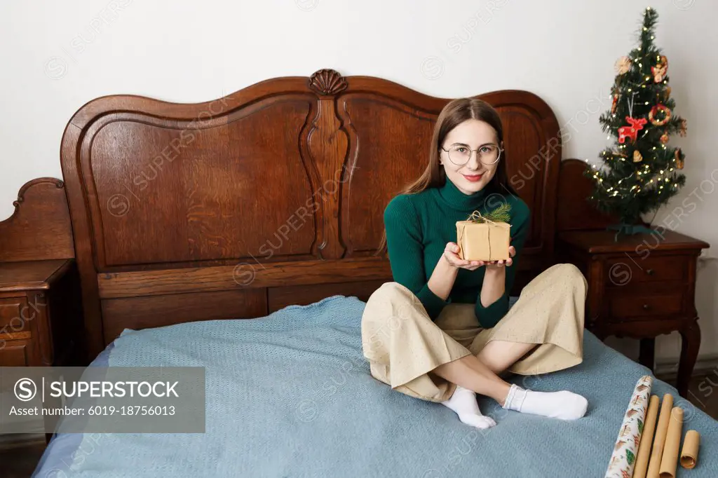 Young woman with a Christmas wrapped gift sitting on the bed