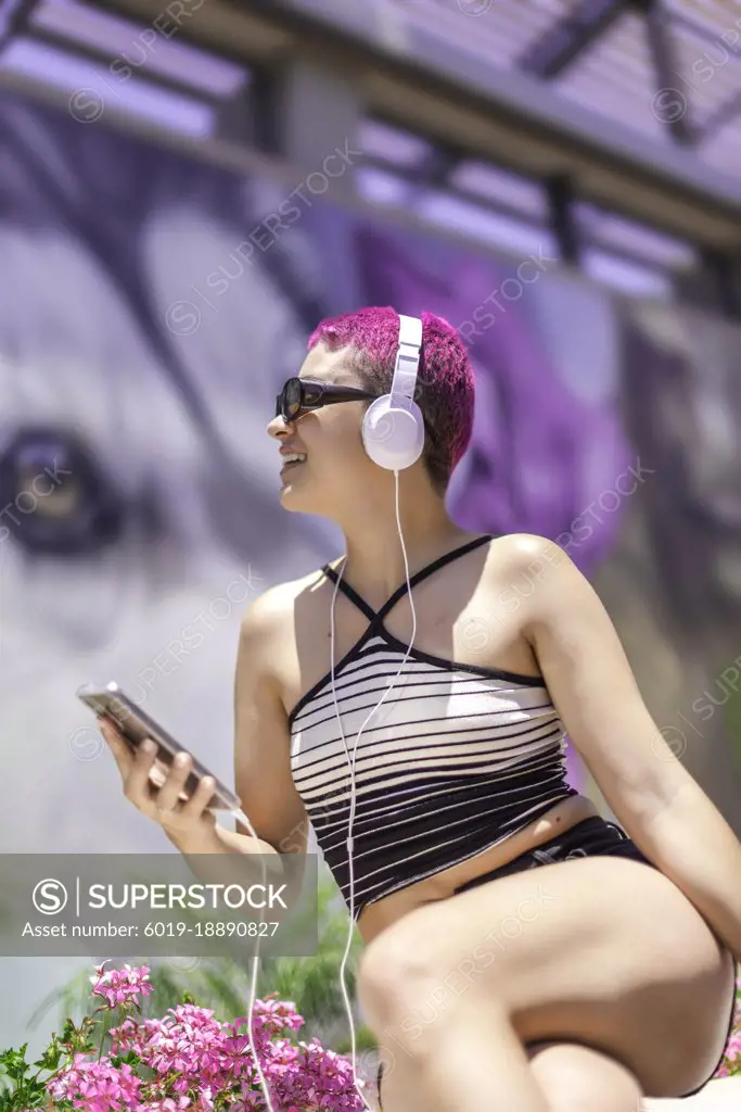 Woman with purple hair and headphones is listening music in her mobile