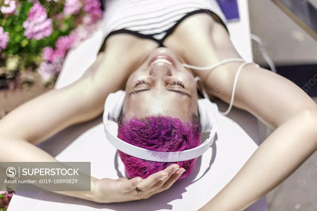 Woman with purple hair and headpones is listening music in her mobile