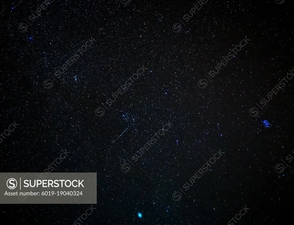 A shooting star streaks across the sky next to the Pleiades