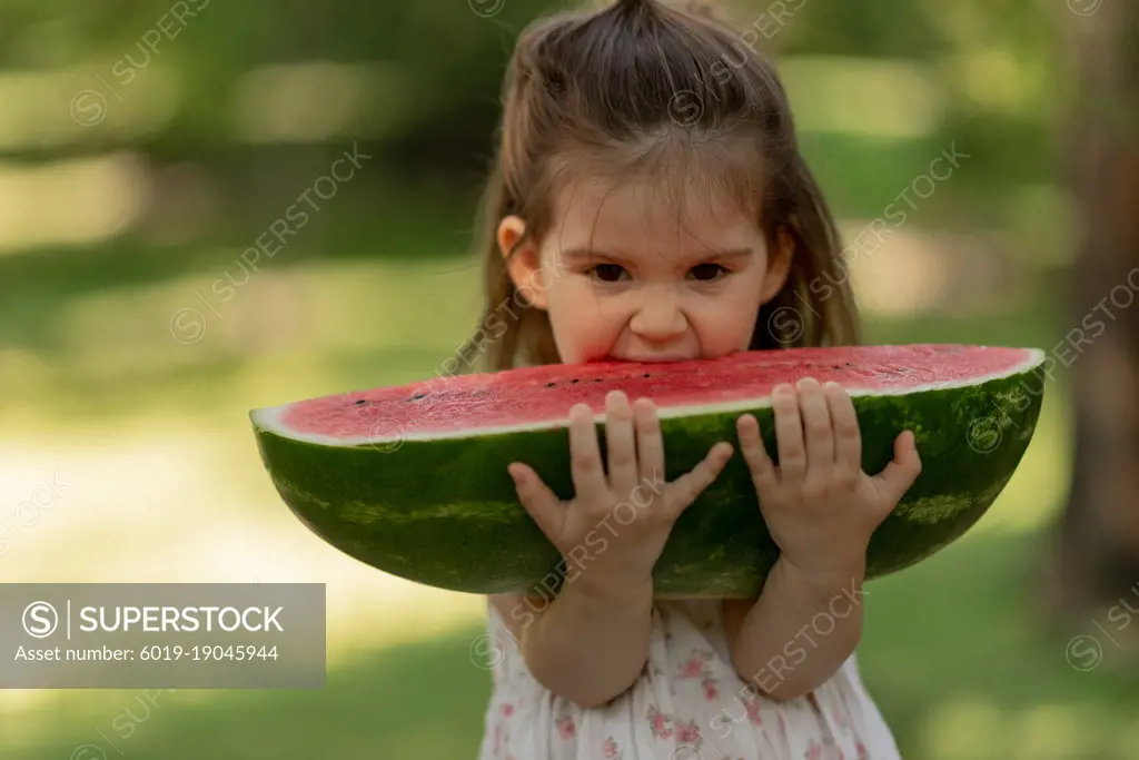 Pretty little girl bitting big piece of juice watermelon