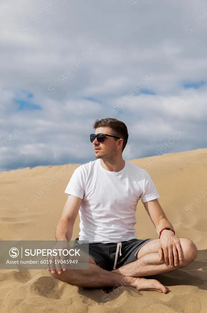 Man in sunglasses sitting in lotus pose in desert on sand