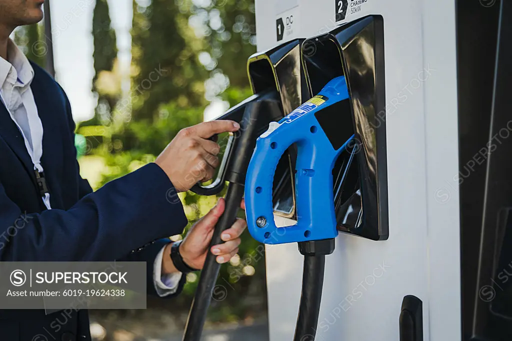 Businessman in a suit refueling his vehicle with an electric charger