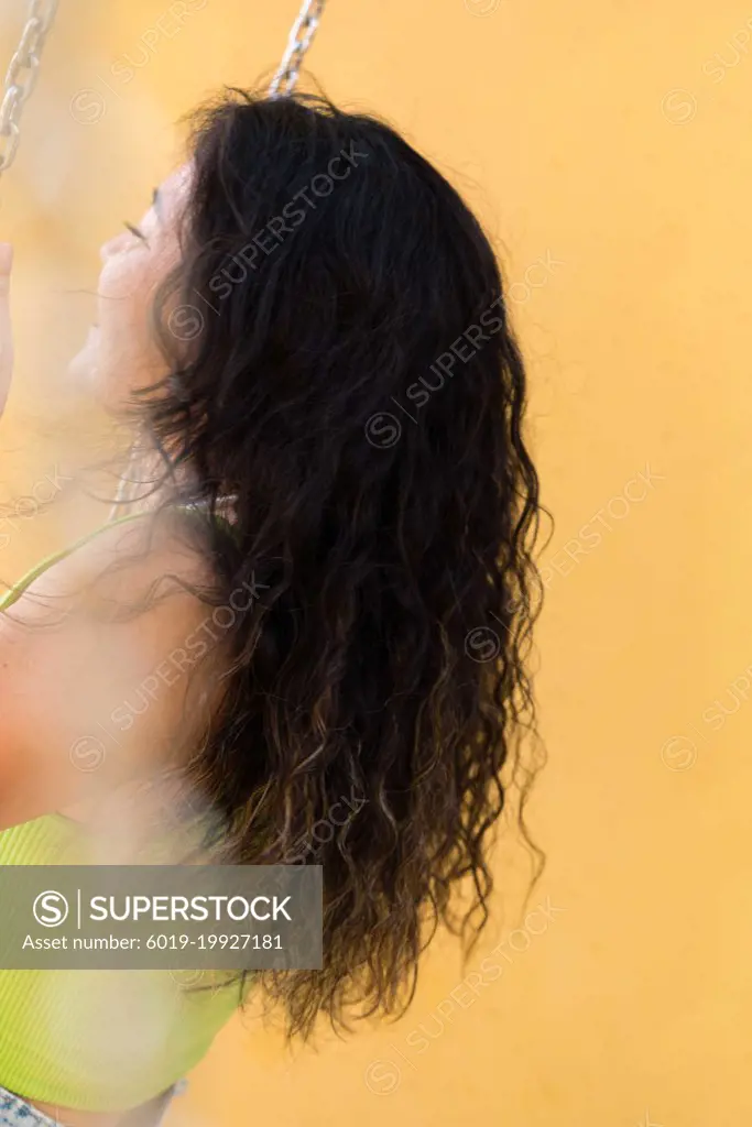 Asian woman sitting on the swings against yellow wall background