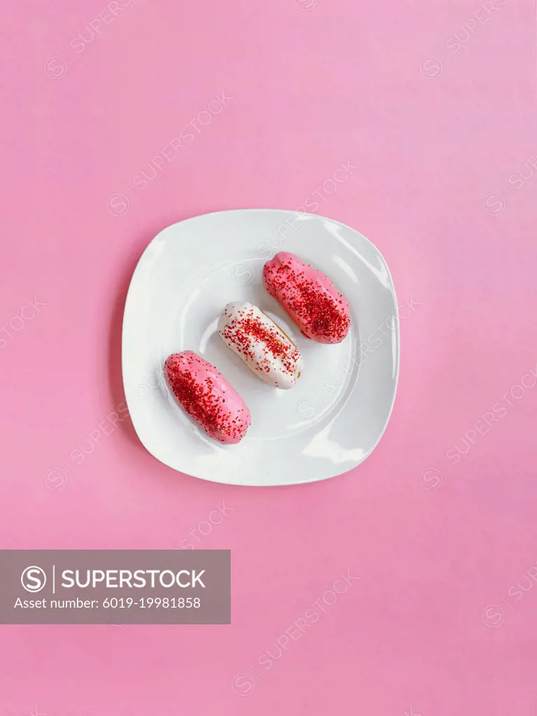 White and pink eclairs on top of a white plate on pink background