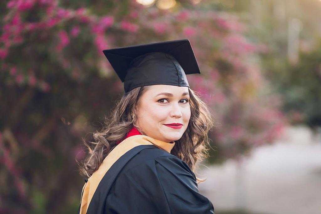 Woman wearing a graduation gown/cap, close to a little smirk.