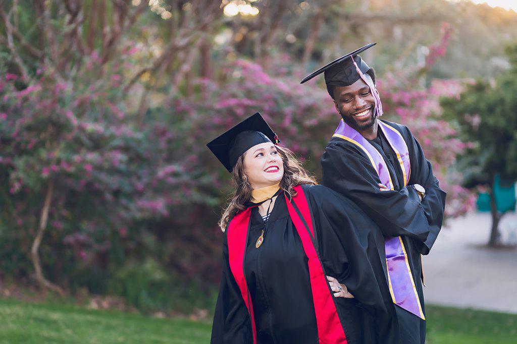 Young man & woman graduating college, wearing a graduation gown/cap.