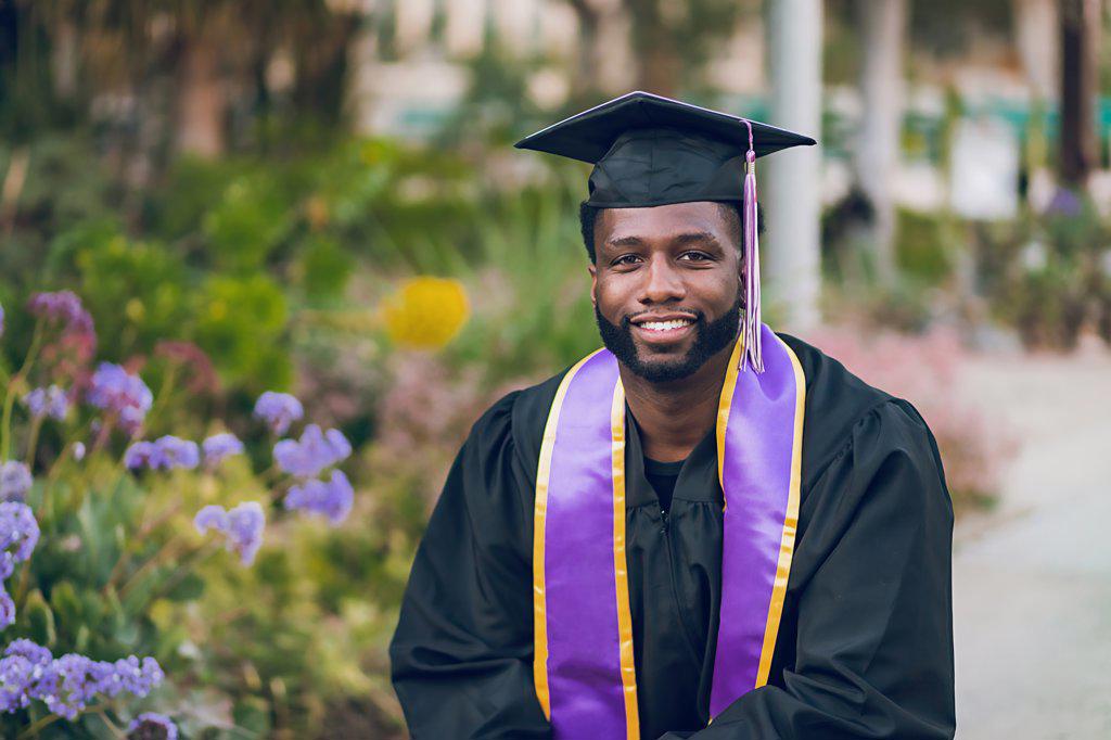 Young man graduating college, wearing a graduation gown/cap.