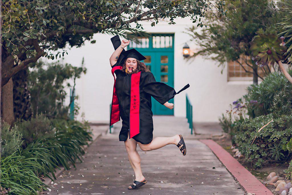 Woman excited to be graduating college, wearing a graduation gown/cap.