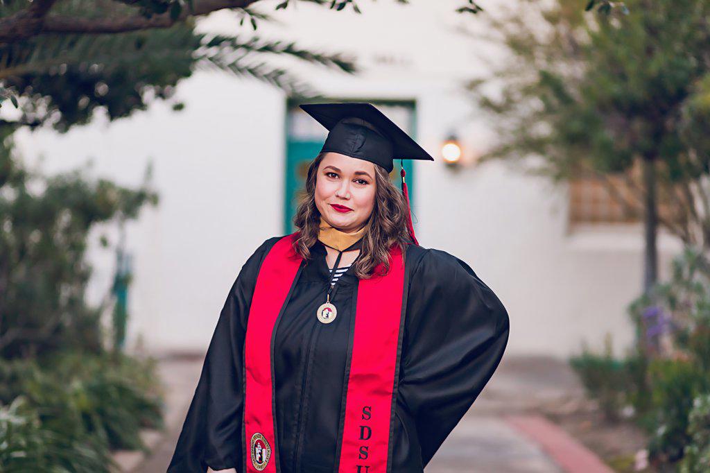 Female millennial graduating college, wearing a graduation gown/cap.