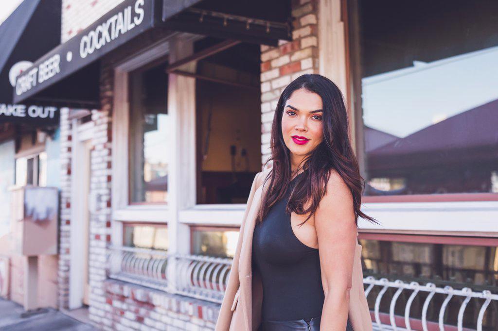 Serious woman standing in front of restaurant with brick walls.