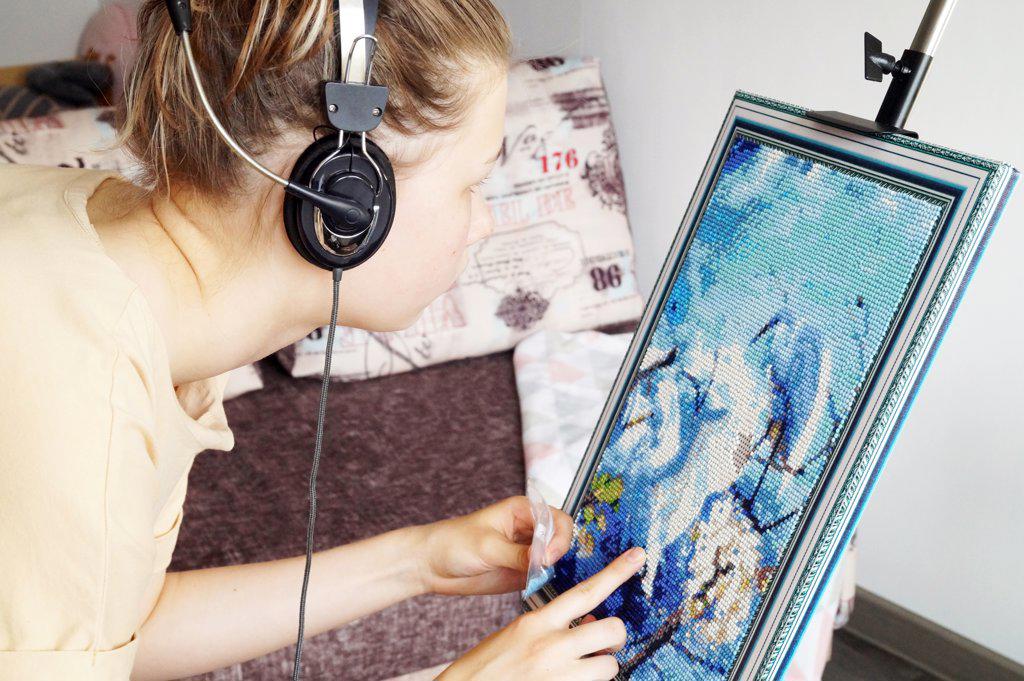 A teenage girl collects a diamond mosaic on an easel