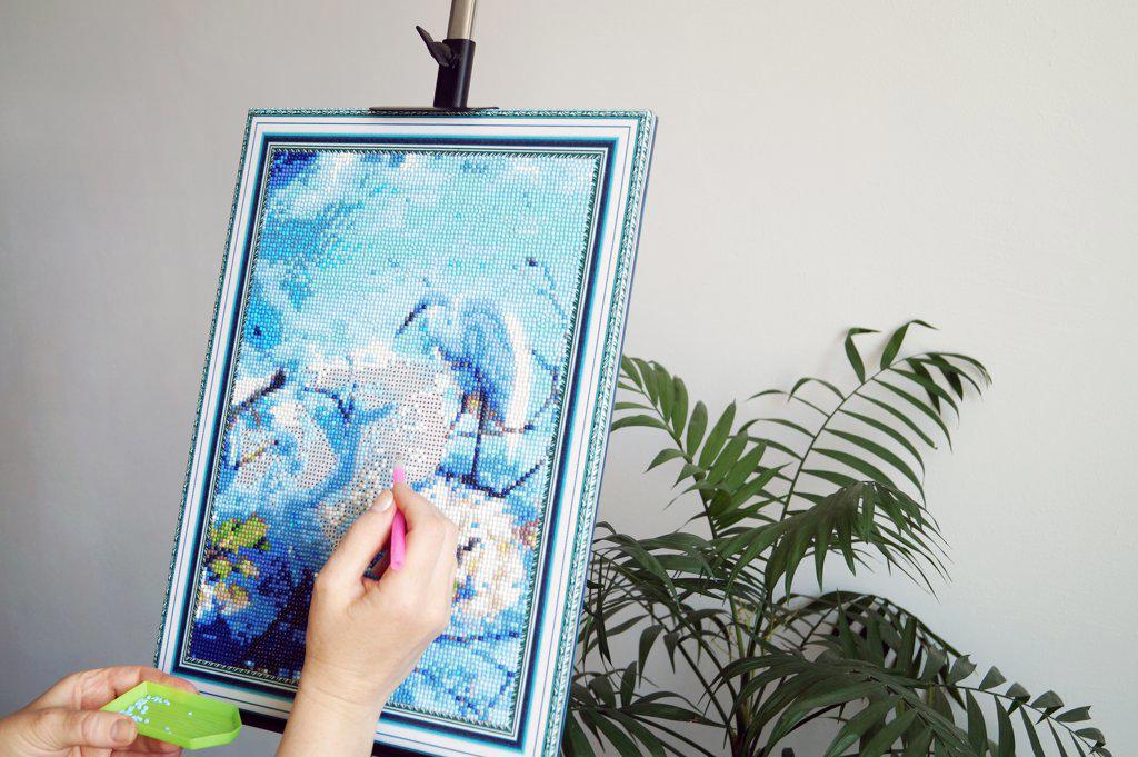 A teenage girl collects a diamond mosaic on an easel