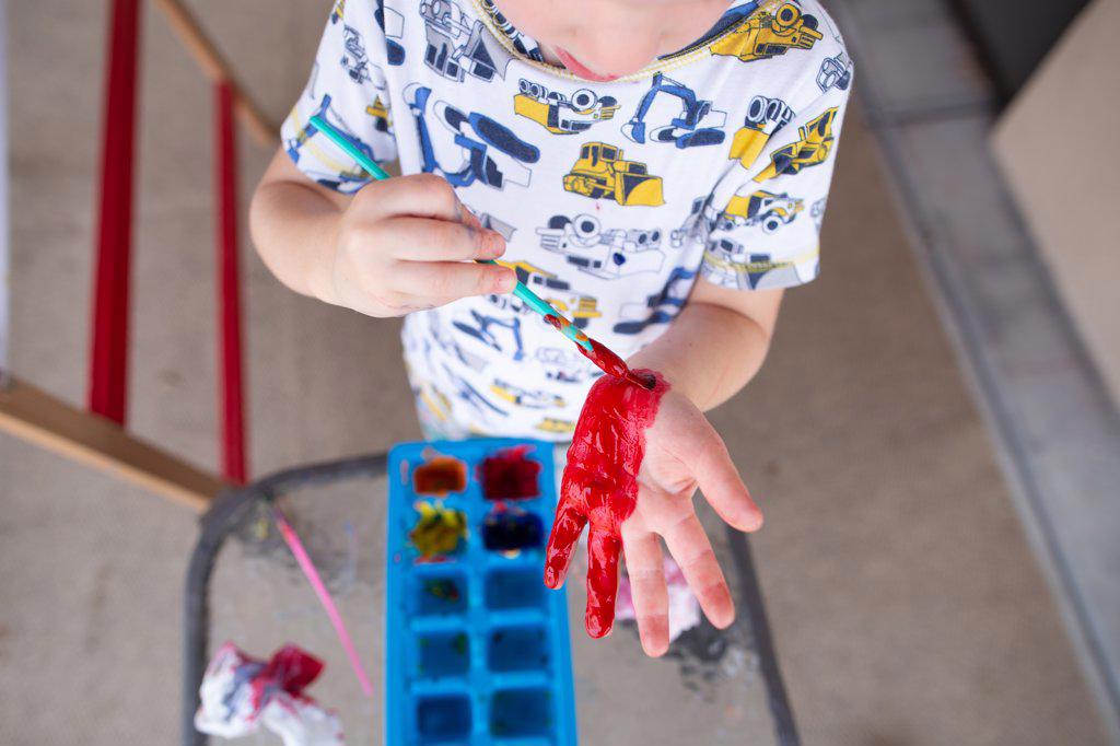 Young Caucasian boy in pajamas playing outside with red finger paint