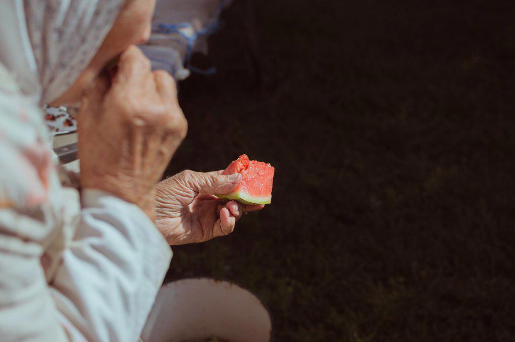 Old woman eats juicy red watermelon in sunlight, copy space