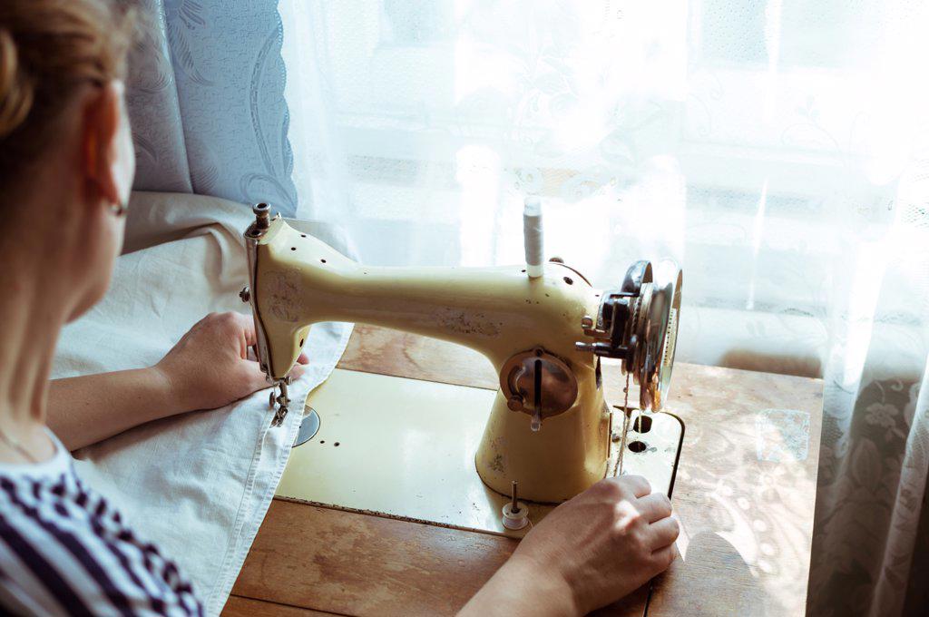 Woman sews on old retro sewing machine at home