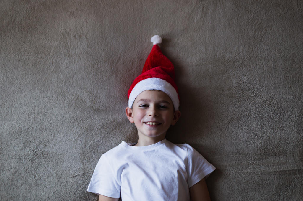 High angle view boy in a Christmas hat smiling while lying on bed