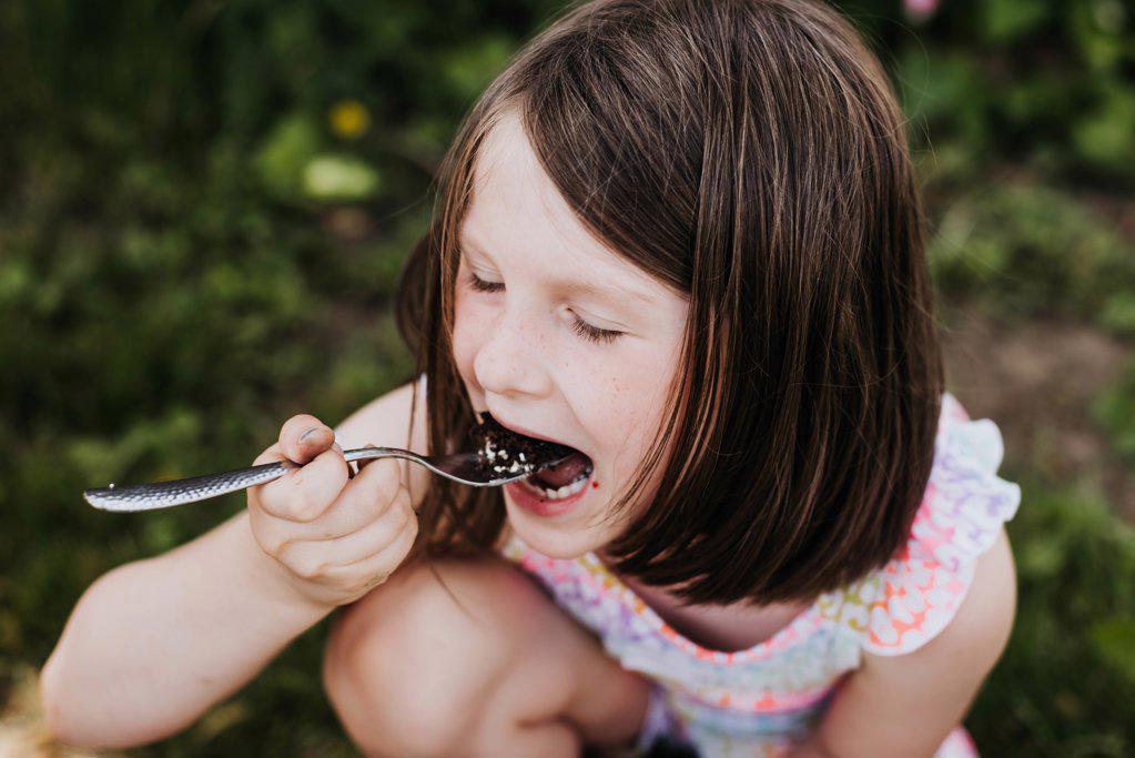 Young girl takes bight of cake outside in grass