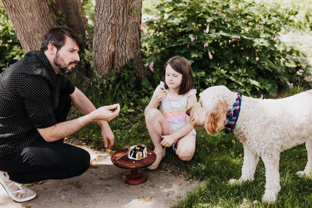 Father and daughter eat cake outside with their goldendoodle