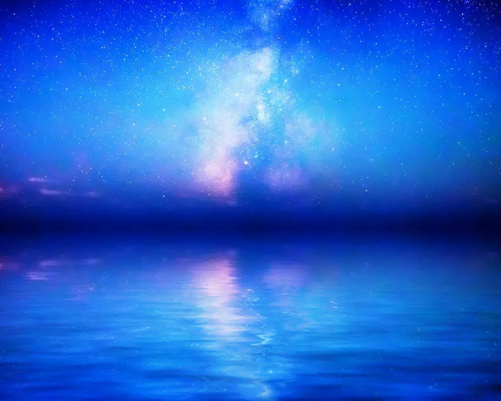 The Milky Way rises above milky blue calm waters