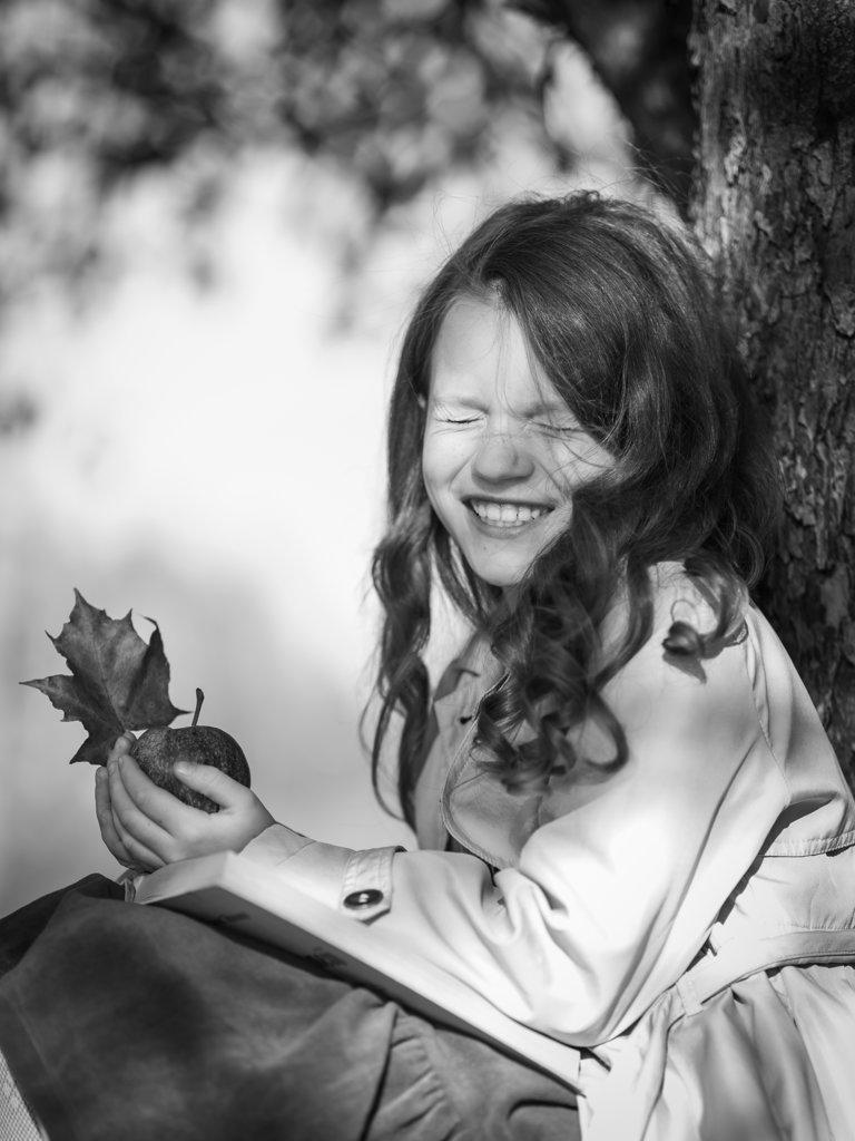 A happy girl in the park with a book and an apple in her hands.