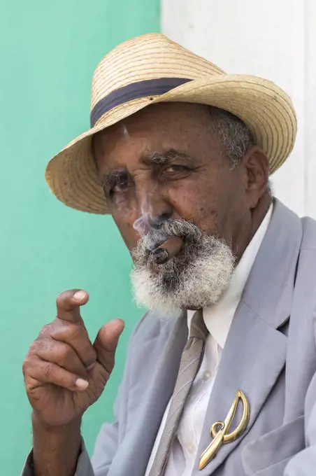 An older well-dressed man smokes a Cuban cigar in Trinidad, Cuba