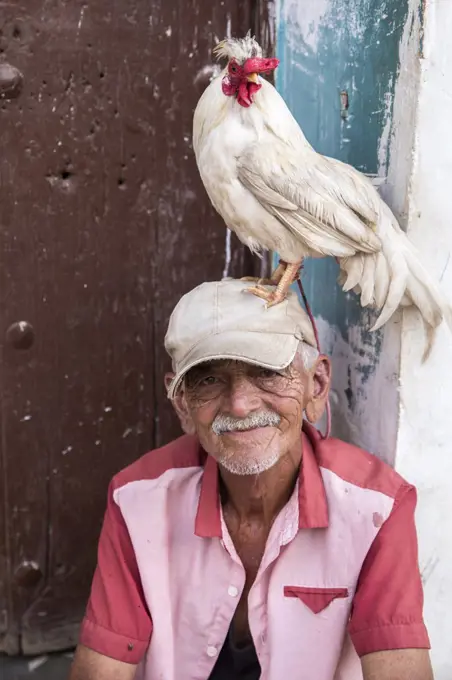 Portrait of an old Cuban man with a pet chicken on his head.