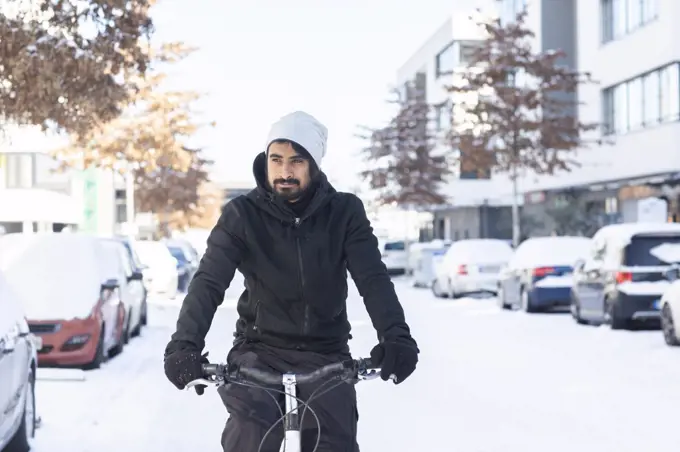 young man with beard riding  bike in snow on a street