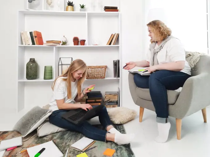 two blond women studying at home laptop and notebooks