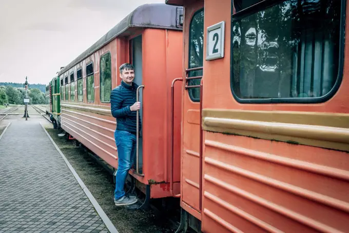 Man stands on the bandwagon of old train of a narrow-gauge railway