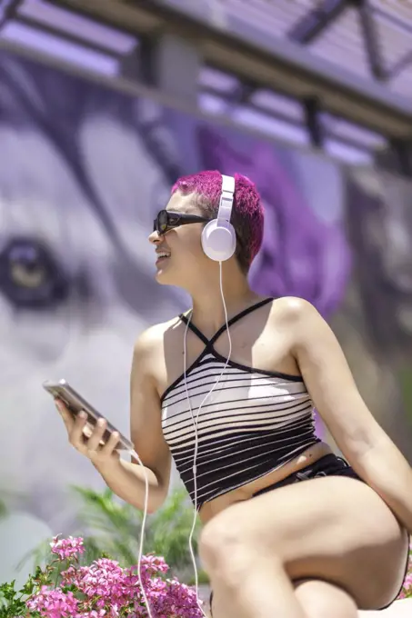 Woman with purple hair and headphones is listening music in her mobile